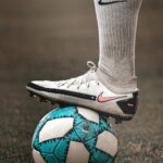 A person in sportswear balancing a blue soccer ball on grassy field.