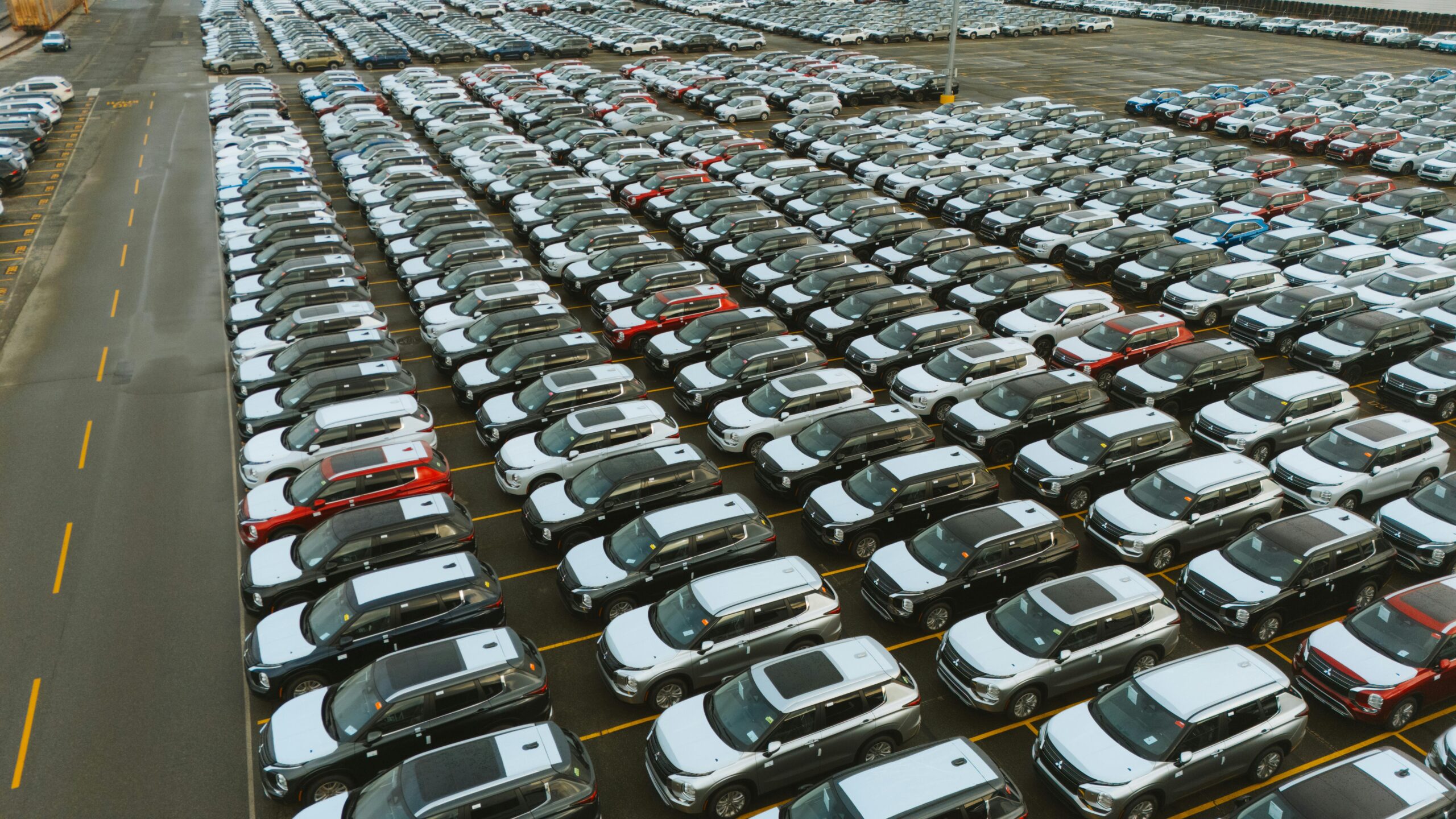 Aerial shot of an extensive car parking lot filled with new vehicles ready for distribution.