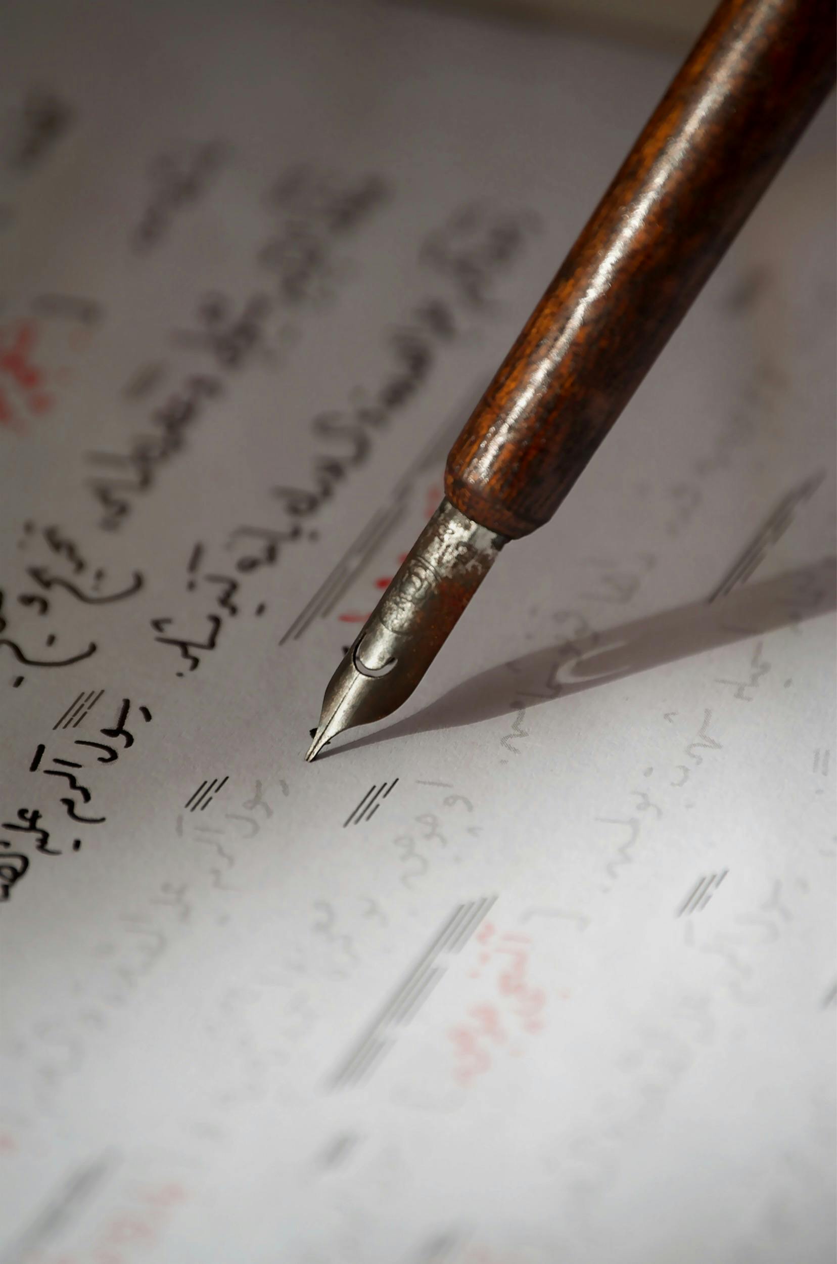 An intimate view of a vintage fountain pen poised over handwritten Arabic text.