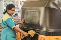 A woman refuels an auto rickshaw at a gas station, showcasing everyday life in India.