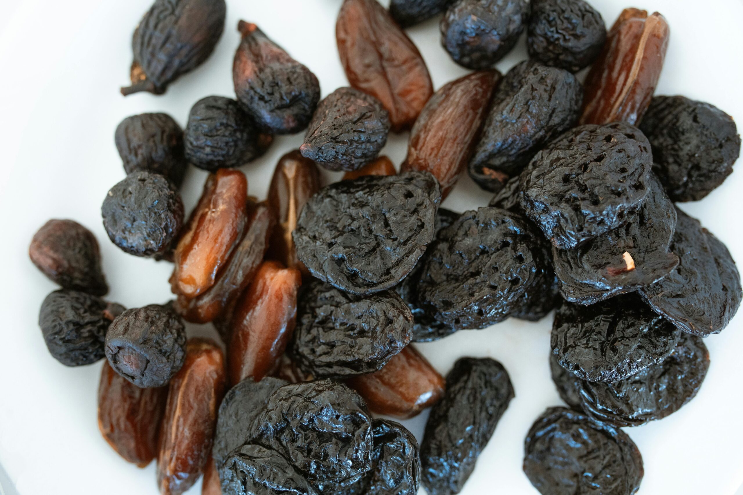 Close-up of assorted dried fruits, including prunes and dates, on a white surface.